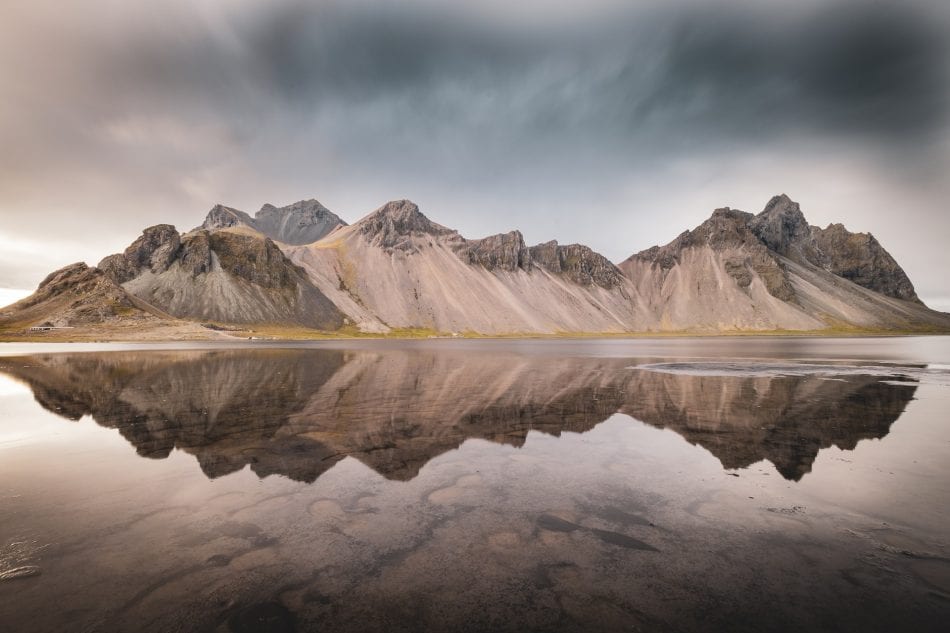 Photo of Icelandic mountain in front of a stormy sky, with water in the foreground reflecting the scene